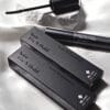 BL Lashes Noir Fix N Hold black tint enhancer with applicator brush and black product packaging arranged on white satin fabric.