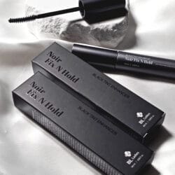 BL Lashes Noir Fix N Hold Black Tint Enhancer BL Lashes Noir Fix N Hold black tint enhancer with applicator brush and black product packaging arranged on white satin fabric.