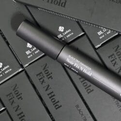 BL Lashes Noir Fix N Hold black tint enhancer tube displayed on top of multiple matching black product boxes.