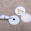 Glue plate with a drop of eyelash extension adhesive, protective glue plate films and an open adhesive bottle on a stone surface.