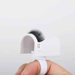 LASH HOLDER (RING)_2 White finger ring lash holder with a curved platform holding black C-curl eyelash extensions for easy access during professional lash application.