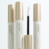 Three Lash Elixir lash and brow essence tubes with champagne-gold caps, displayed alongside an open applicator wand with a white spoolie brush on a clean white background.