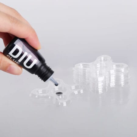 Eyelash extension glue being dispensed from a bottle into a clear plastic multi-well glue tray for professional lash application.