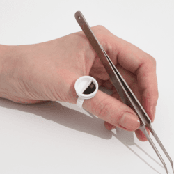 Lash artist holding precision tweezers while wearing a white glue ring for eyelash extension adhesive