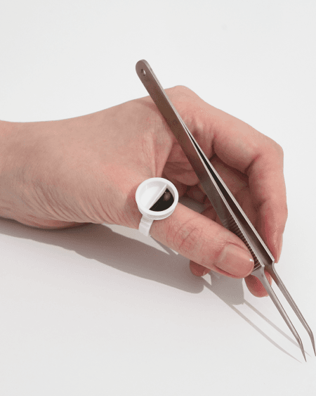 glue-ring-in-use-4x5 Lash artist holding precision tweezers while wearing a white glue ring for eyelash extension adhesive